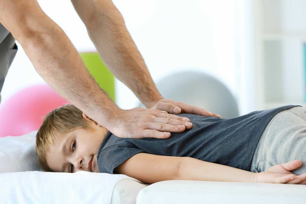 A person applies an ice pack to their neck while sitting in a bright, comfortable living room.